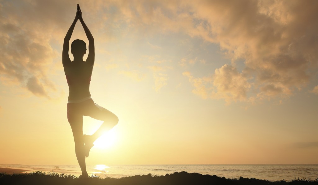 Young woman silhouette practicing yoga on the sea beach at sunset