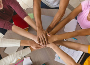 Multiracial teenagers joining hands together in cooperation, preparing common academic project, top view