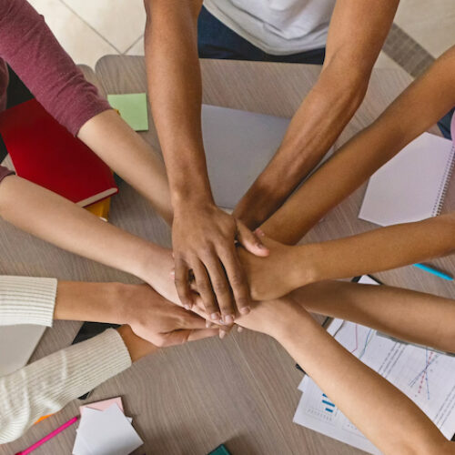 Multiracial teenagers joining hands together in cooperation, preparing common academic project, top view