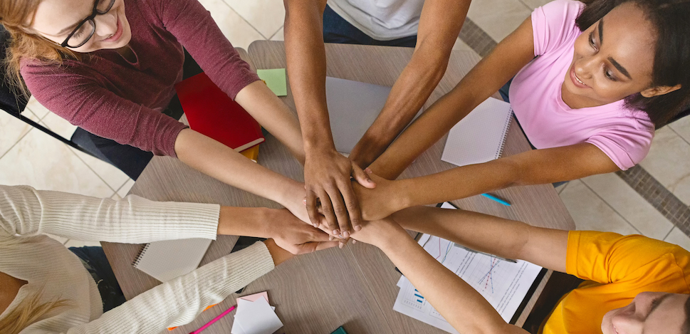 Multiracial teenagers joining hands together in cooperation, preparing common academic project, top view
